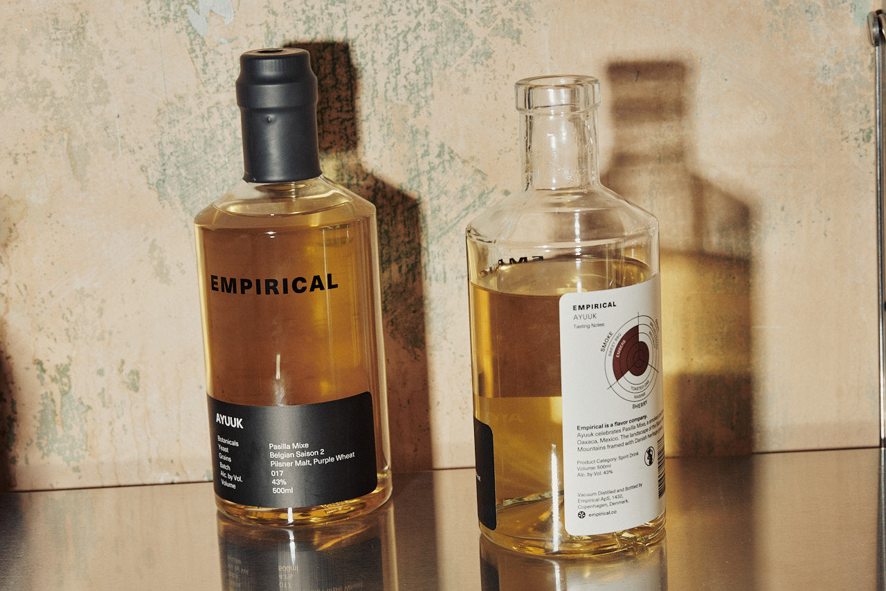 Empirical Ayuuk and a sister bottle photographed side-by-side on a stone bar