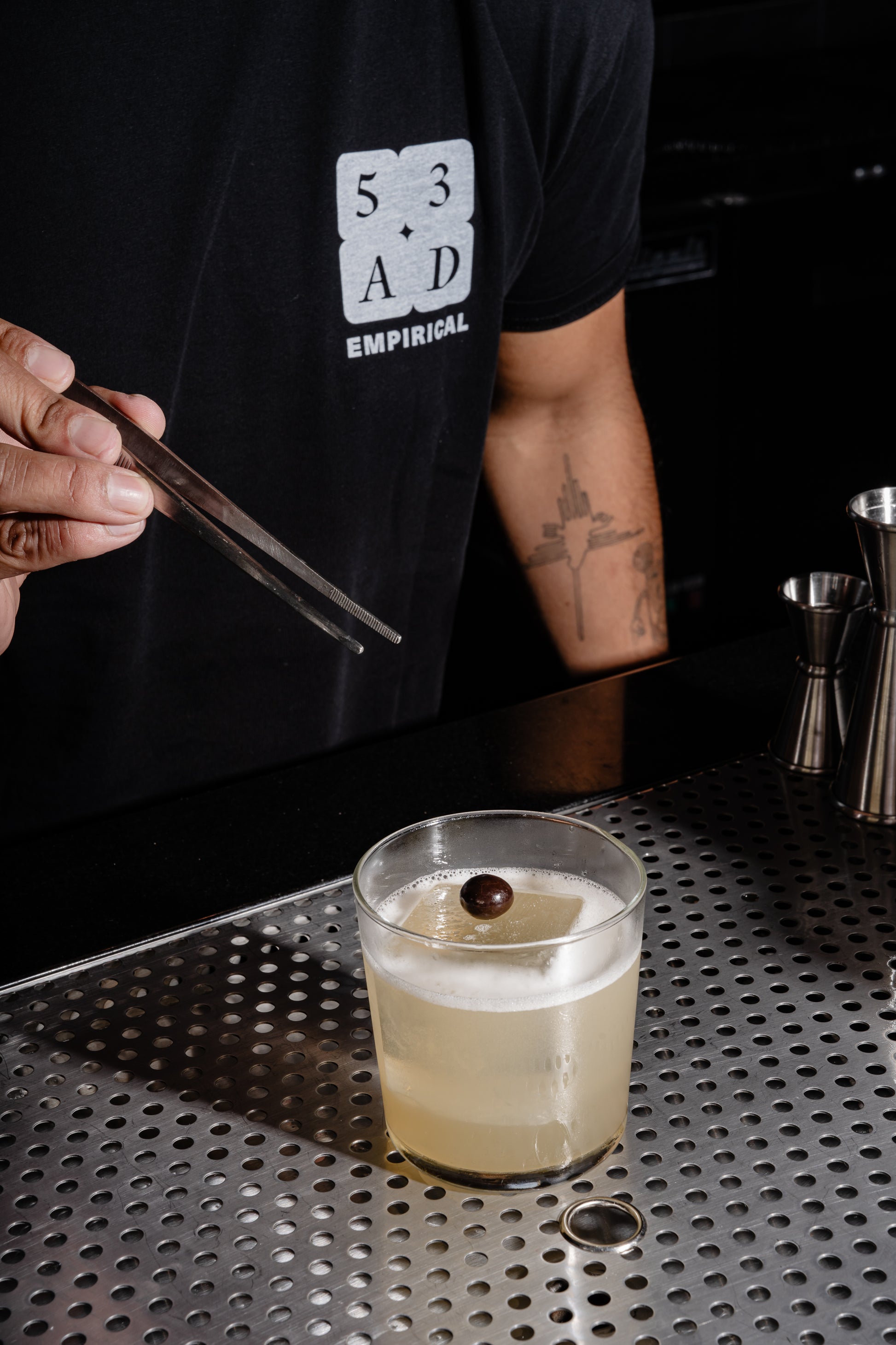 Bartender wearing the 53AD Empirical staff tee, garnishing a sour with a brandied cherry