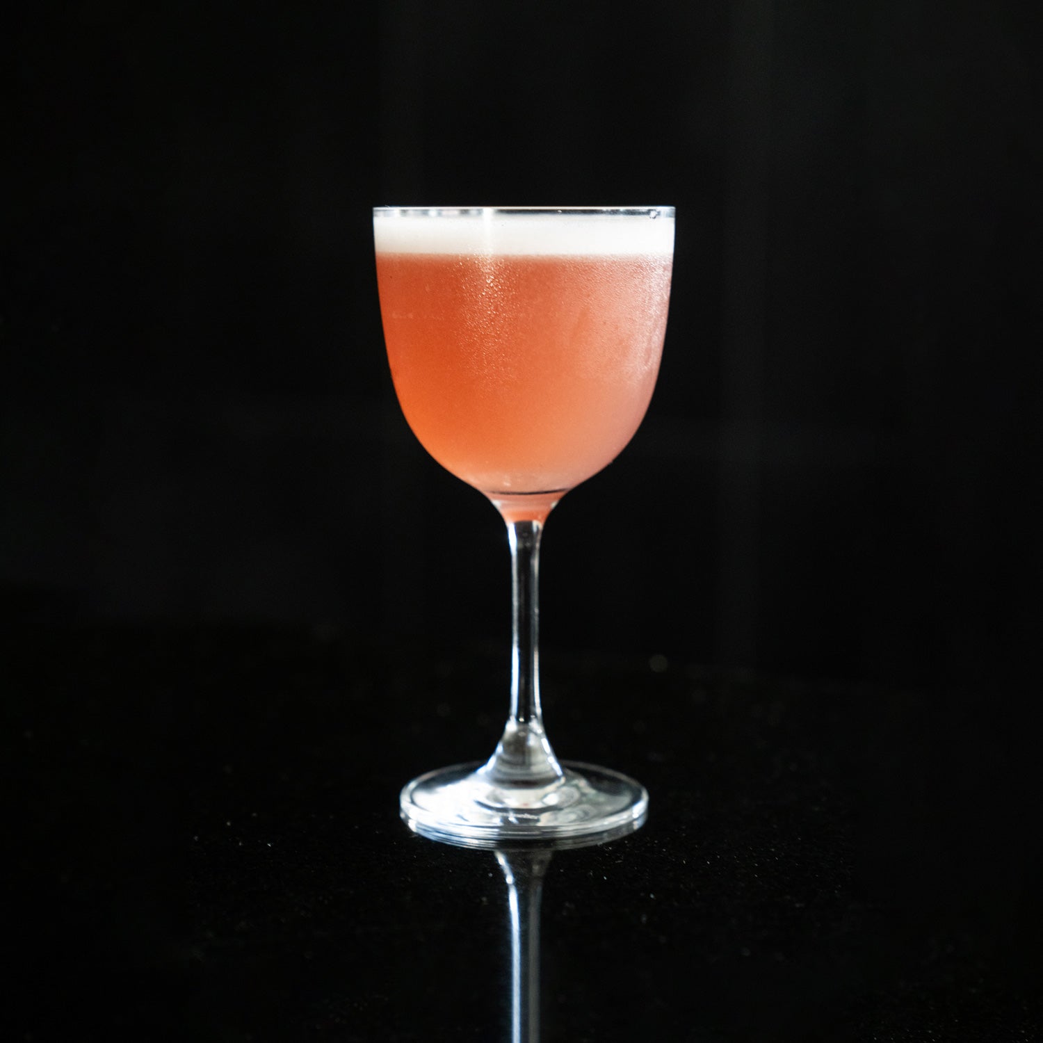 Pink-foam cocktail in a Nick & Nora glass on a black backdrop — Cilantro & Centerbe