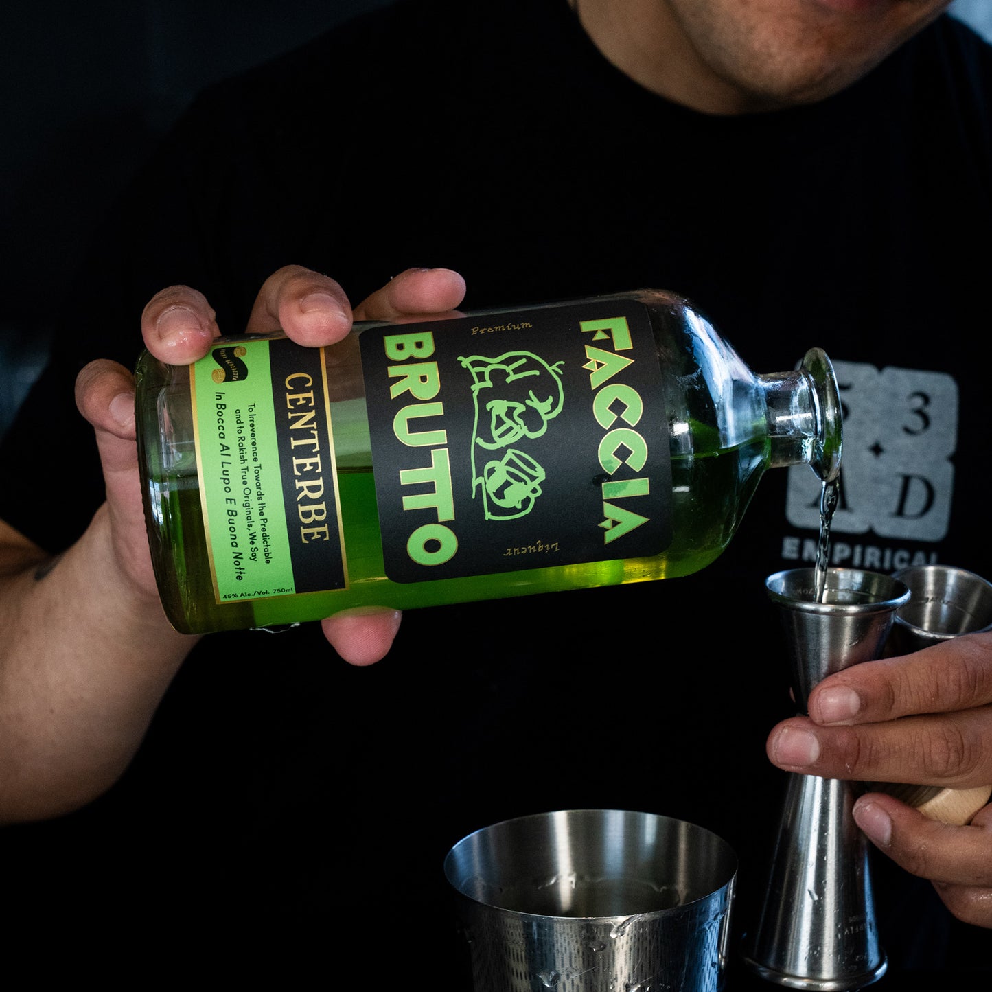 Bartender pouring Faccia Brutto Centerbe alongside Empirical Cilantro into a jigger