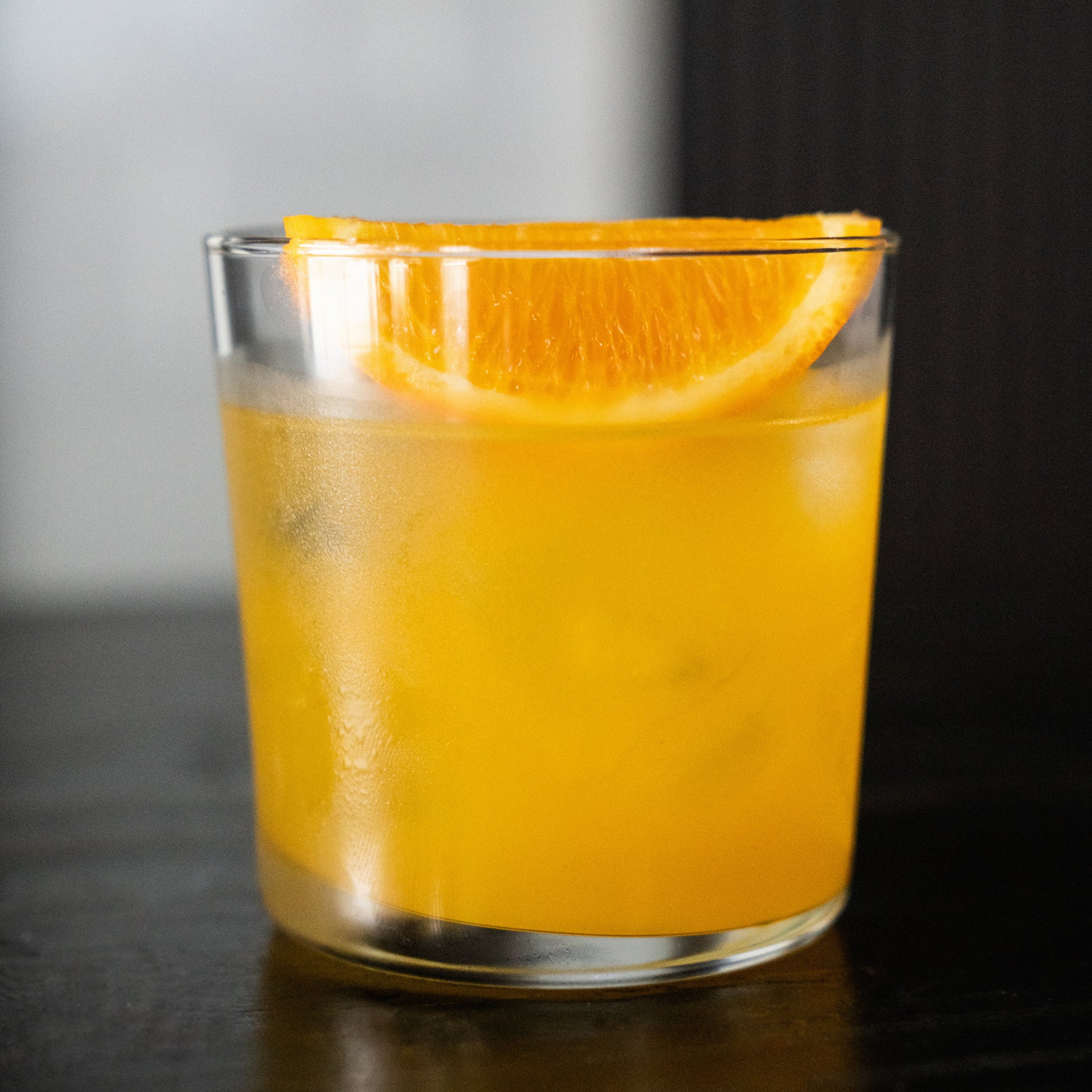 Cilantro & Mango cocktail in a rocks glass with lime wedge on a wood bar