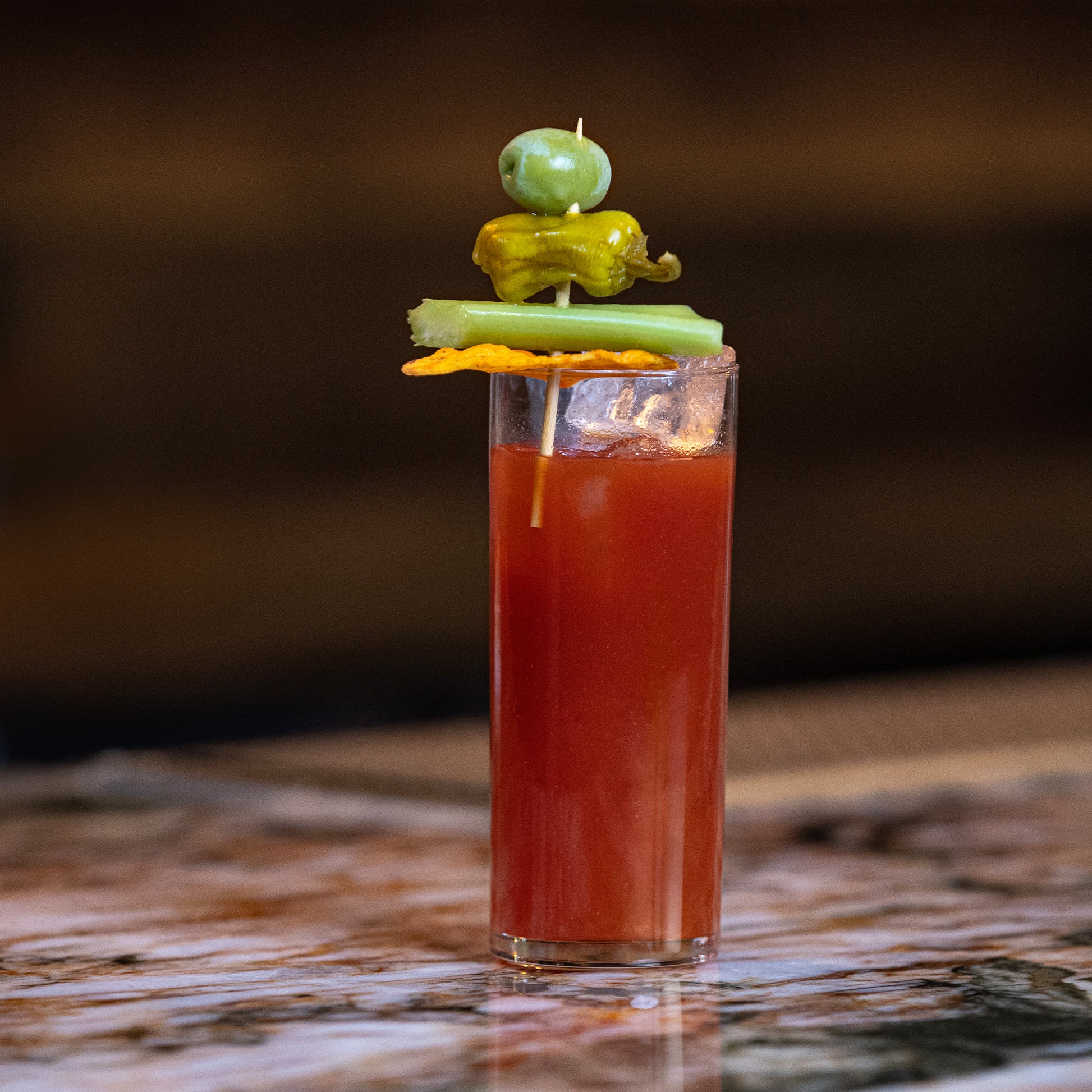 Doritos x Empirical bloody mary in a tall glass with celery, olive, and pepperoncini garnish