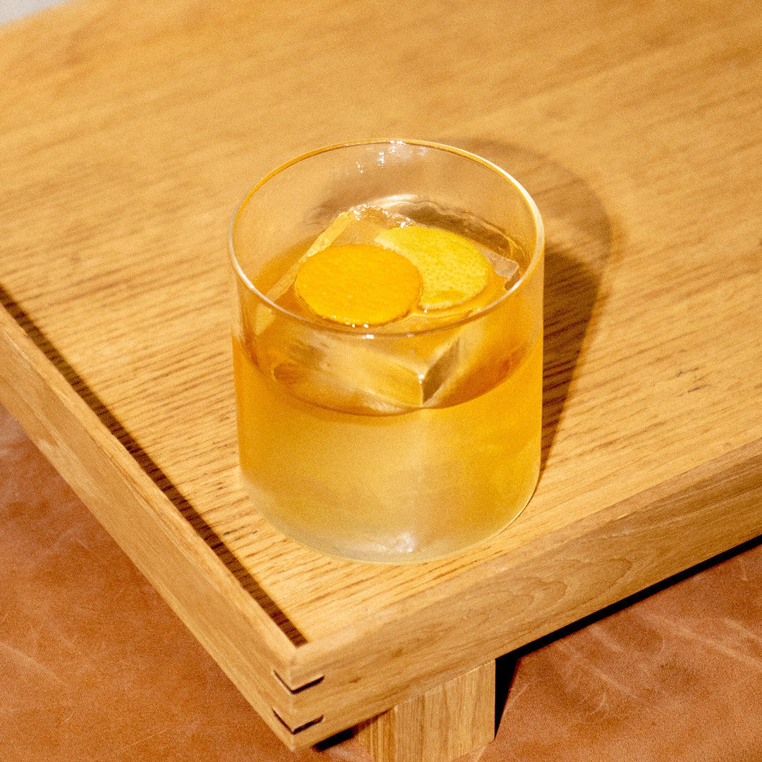 Empirical Ayuuk Old Fashioned in a rocks glass with orange peel garnish on a wood table