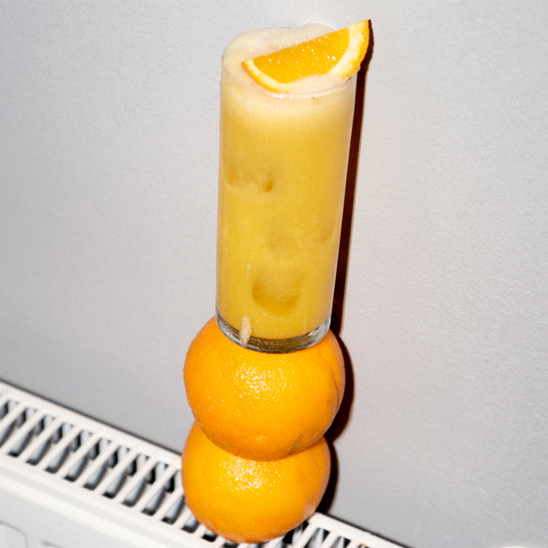 Symphony 6 Orange cocktail in a tall glass perched on a stack of oranges