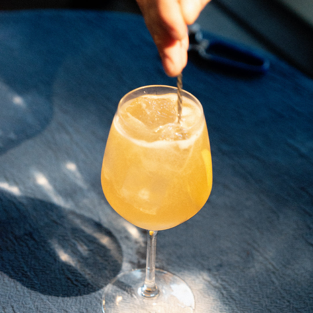 Symphony 6 sour-style cocktail in a wine glass on a denim-blue surface