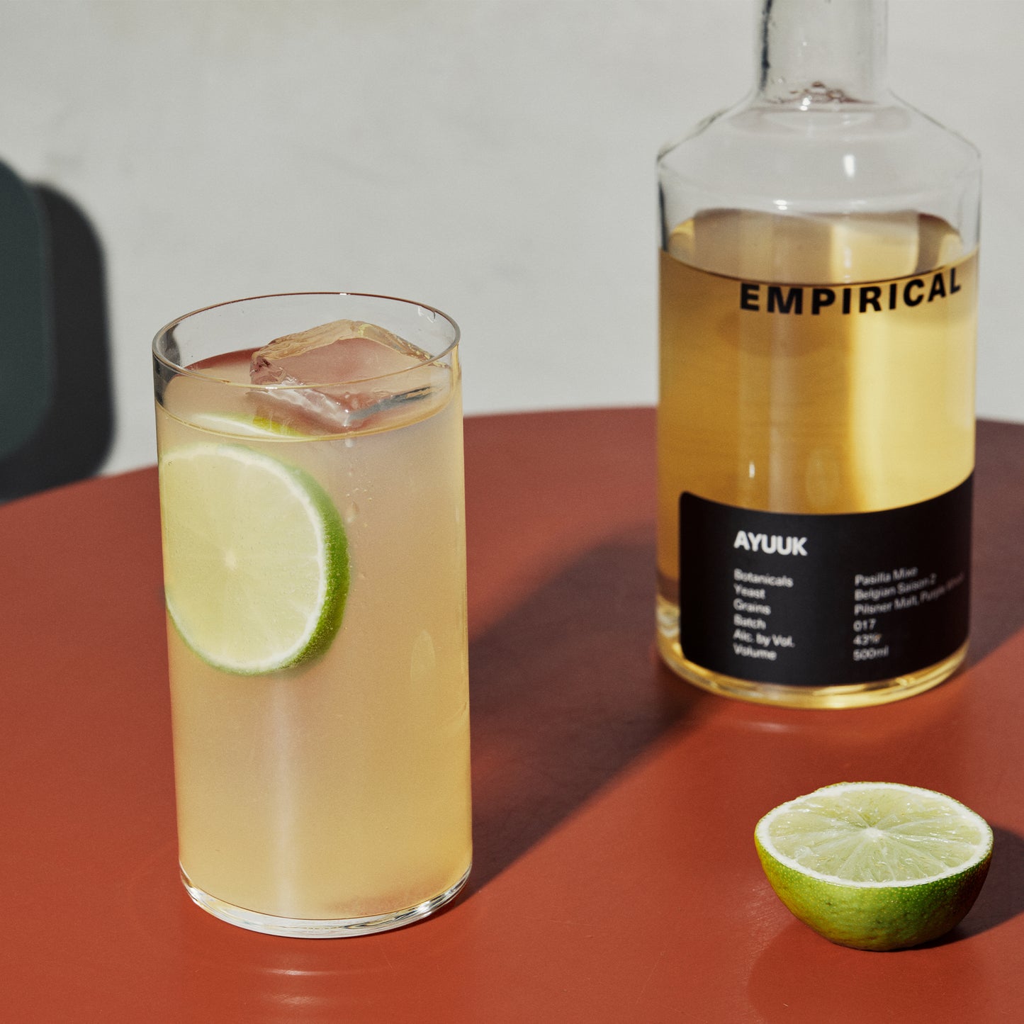 Ayuuk highball with lime alongside the Empirical Ayuuk bottle on a terracotta surface