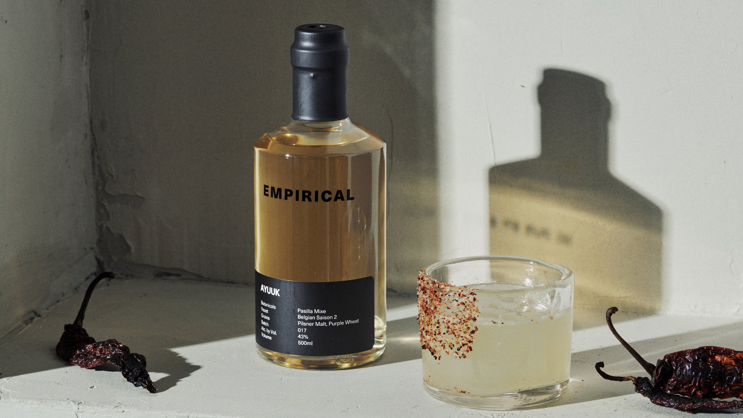 Empirical Ayuuk bottle with a chili-rimmed margarita and dried chilis on a sunlit ledge