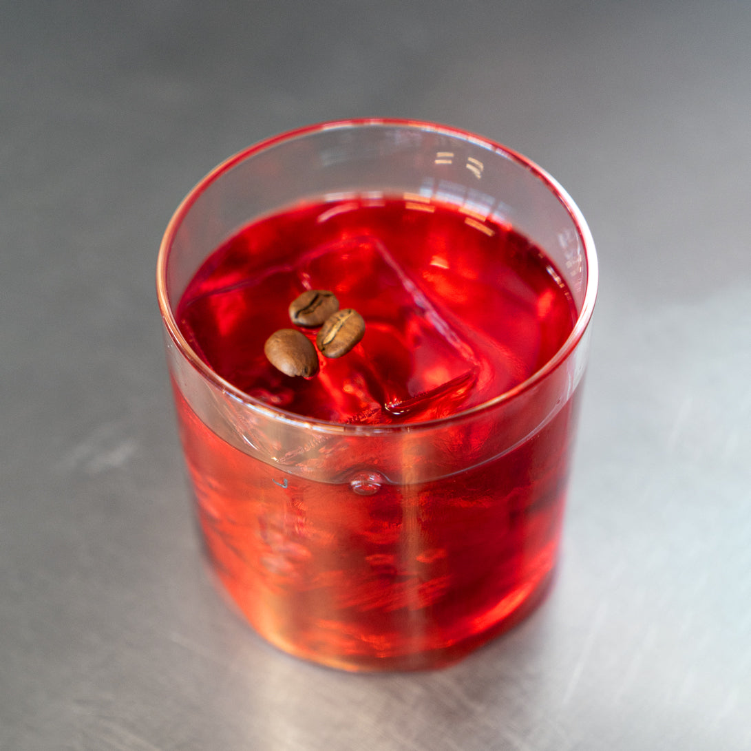 Bright red Ayuuk cocktail in a rocks glass garnished with two coffee beans