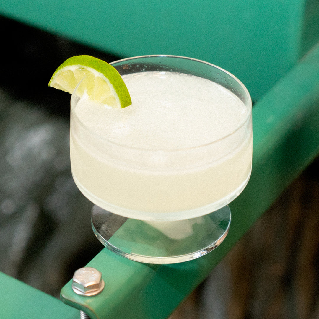 Soka daiquiri in a coupe glass with lime wedge, on a green metal bench