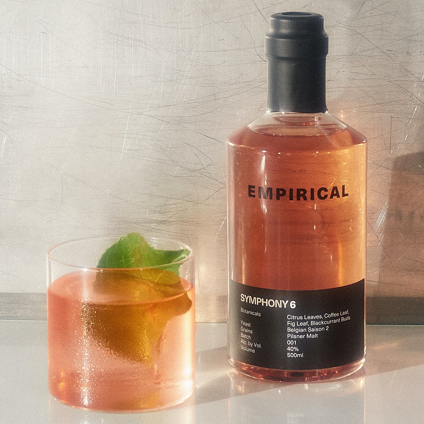 Symphony 6 cocktail in a rocks glass with fresh fig leaves alongside the bottle