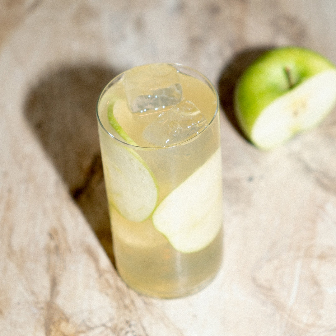 Soka & Apple cocktail in a highball glass with apple slices, on rough wood