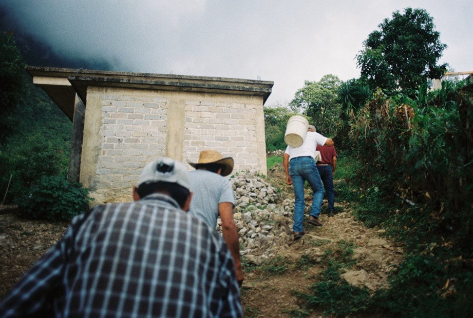 Ayuuk producers walking up a stone path toward a fermentation hut in Oaxaca